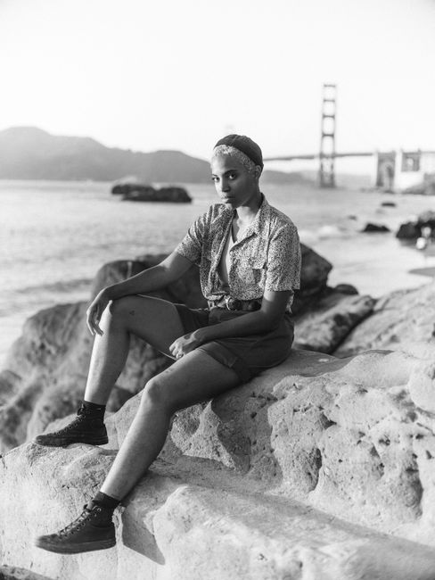 Black and white portrait of a stylish woman sitting by the Golden Gate Bridge.