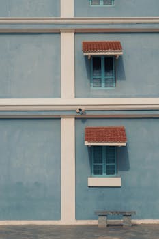 A blue building facade with symmetrical windows and tiles, exuding minimalist style.