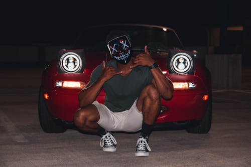 Man Wearing Mask Crouching in Front of Red Car