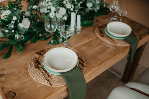 Stylish wooden dining table setup with green accents and floral decor.