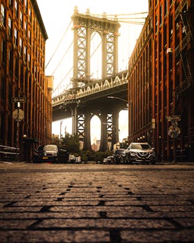 Captured in Dumbo, Brooklyn, this view highlights the iconic Brooklyn Bridge framed by urban architecture at sunset. by Anas Hinde