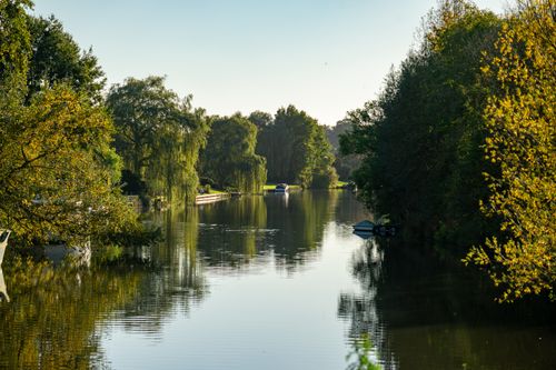 Free Peaceful river scene surrounded by lush autumn trees and boats under a clear sky. Stock Photo