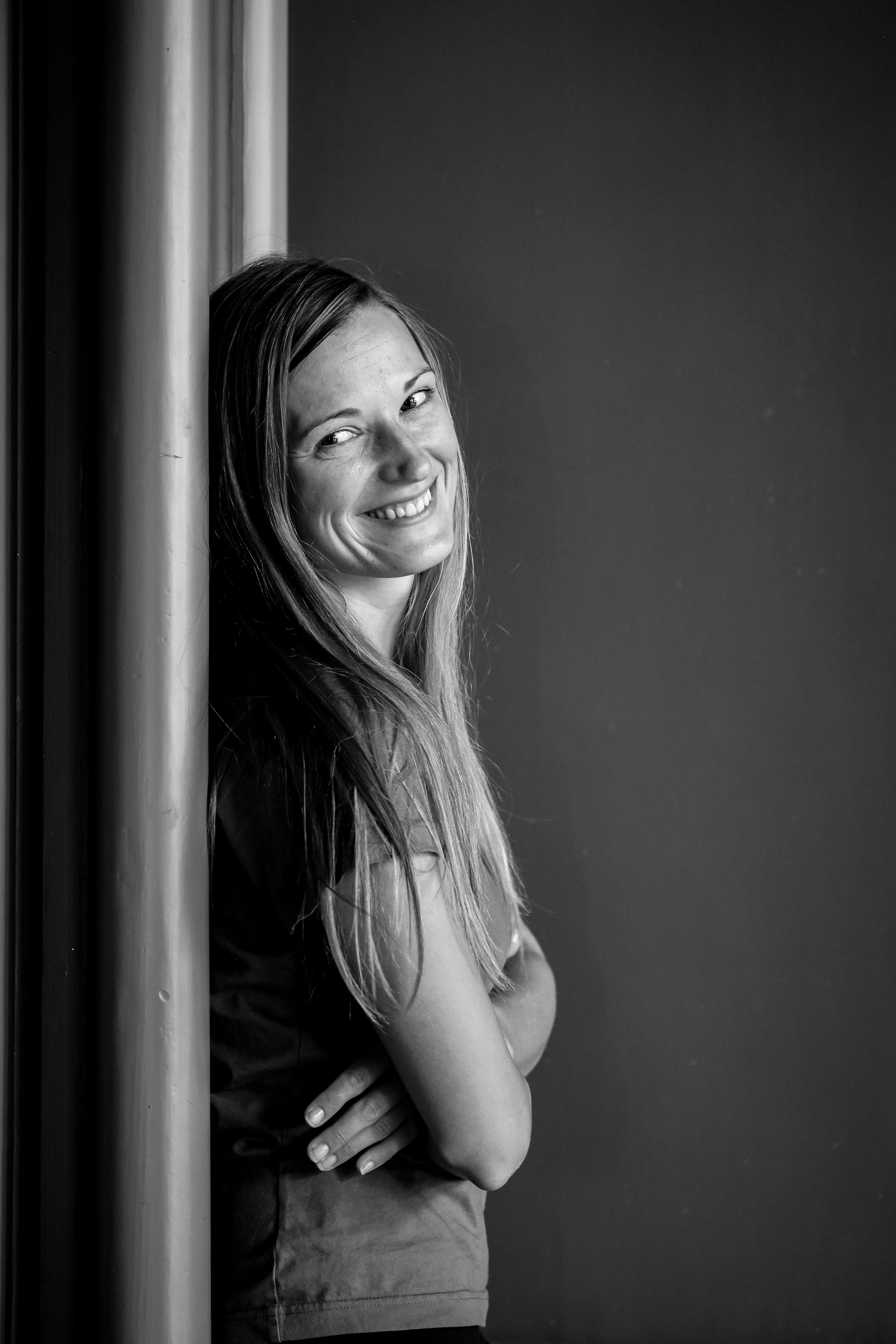 Black and white portrait of a woman smiling while leaning against a wall.