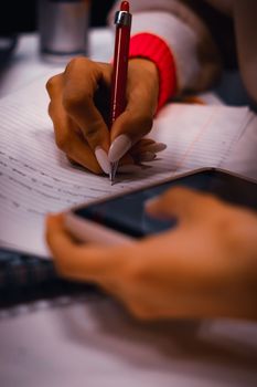 Close-up of a woman's hand writing while holding a smartphone, capturing modern multitasking.