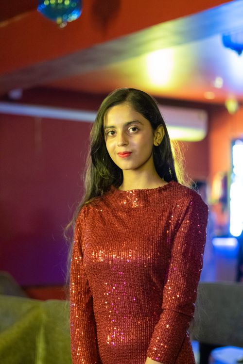 Free Stylish portrait of a young woman wearing a shimmering red dress indoors with ambient lighting. Stock Photo