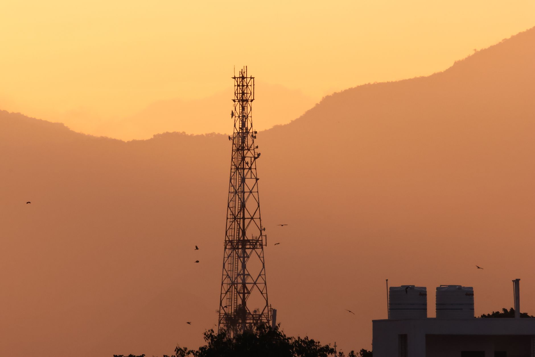 Silhouette of a communication tower against a vibrant sunset in Tamil Nadu, India.