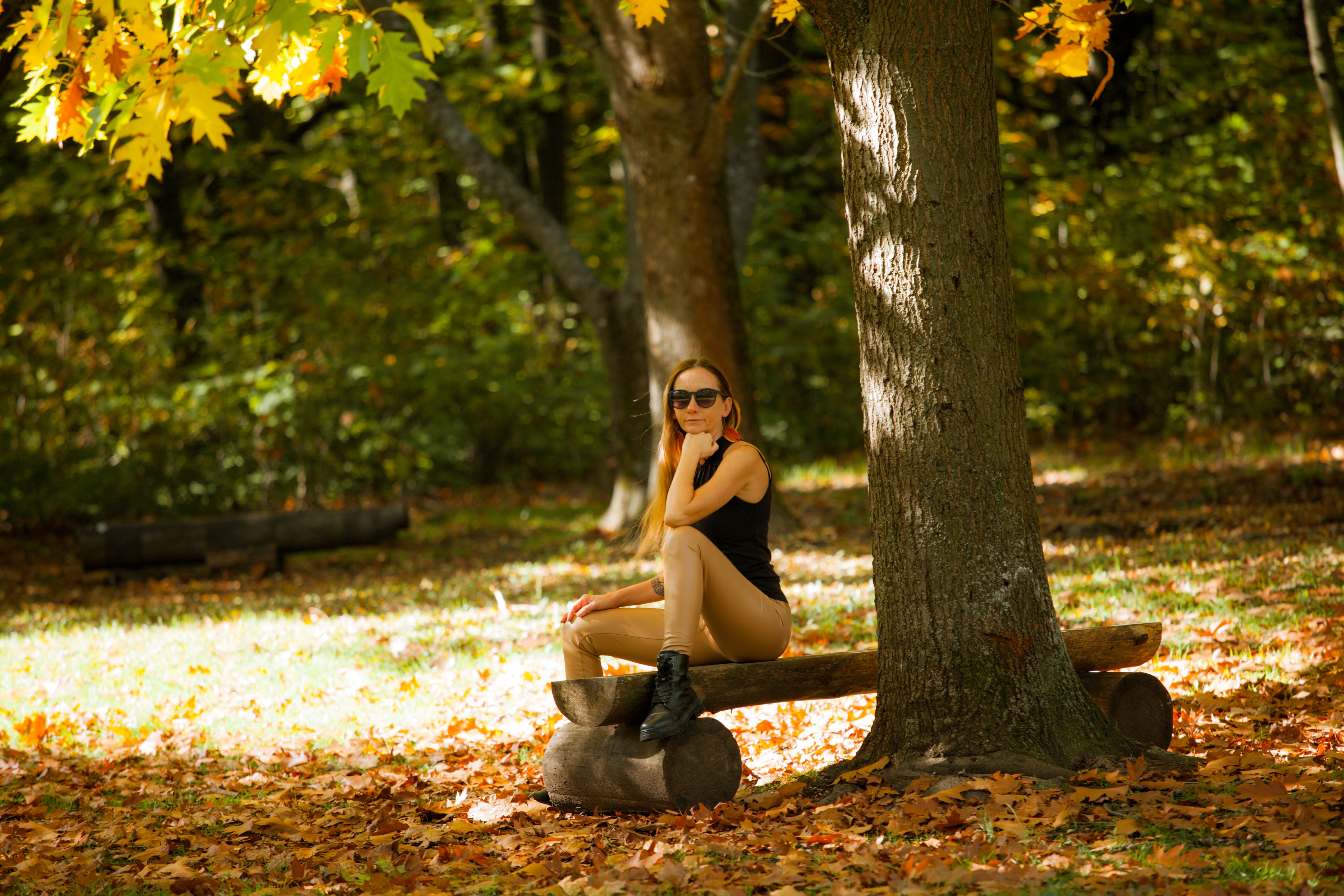 A woman enjoys a sunny autumn day, sitting on a log bench surrounded by colorful leaves.