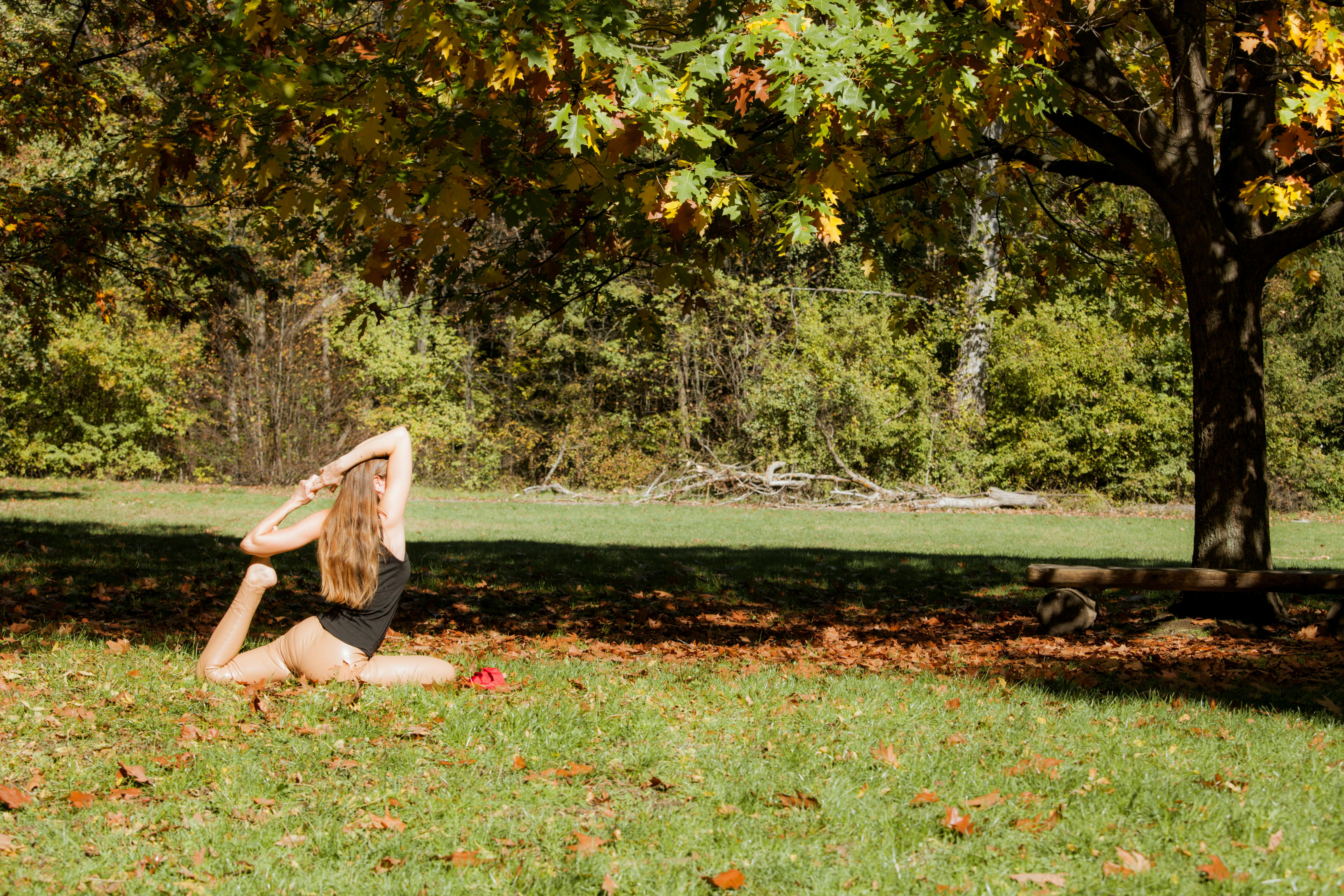 A woman practices yoga in a serene autumn park setting, surrounded by colorful trees.
