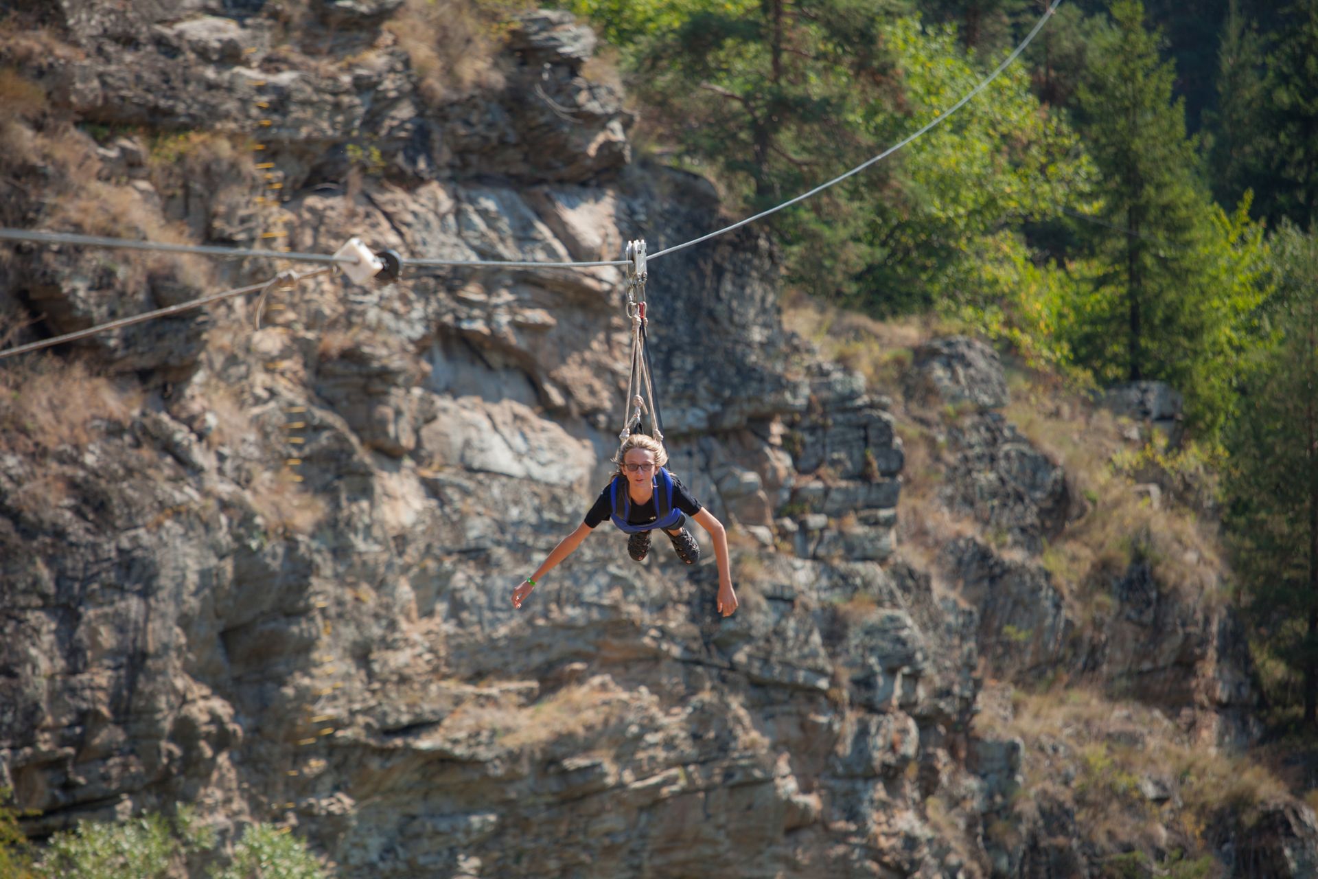 An adventurous person ziplining over a scenic rocky canyon on a sunny day.