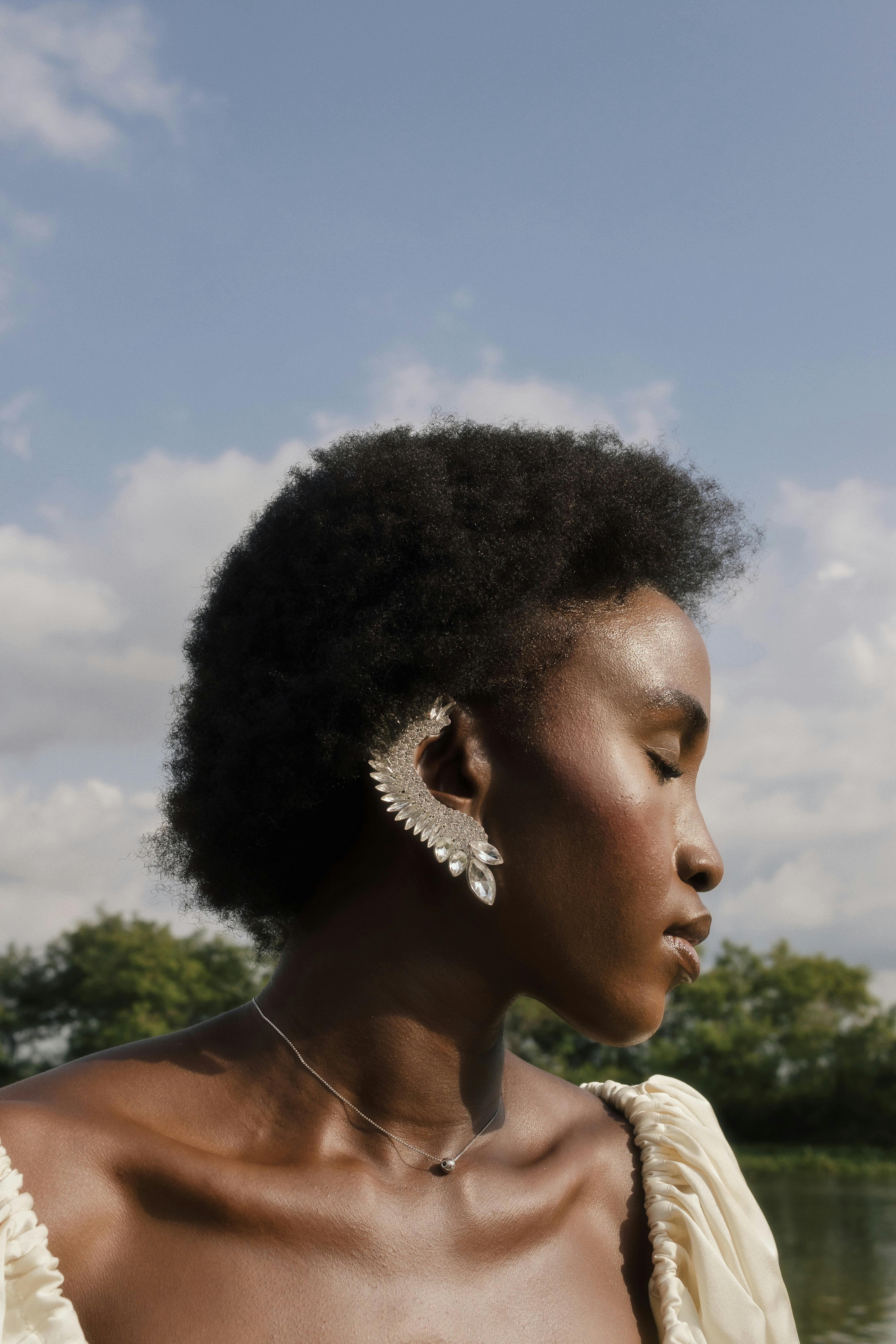A serene portrait of a woman with elegant earrings by a lake in Nigeria.