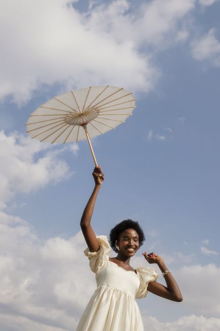 African woman holding a parasol under blue skies in Nigeria.