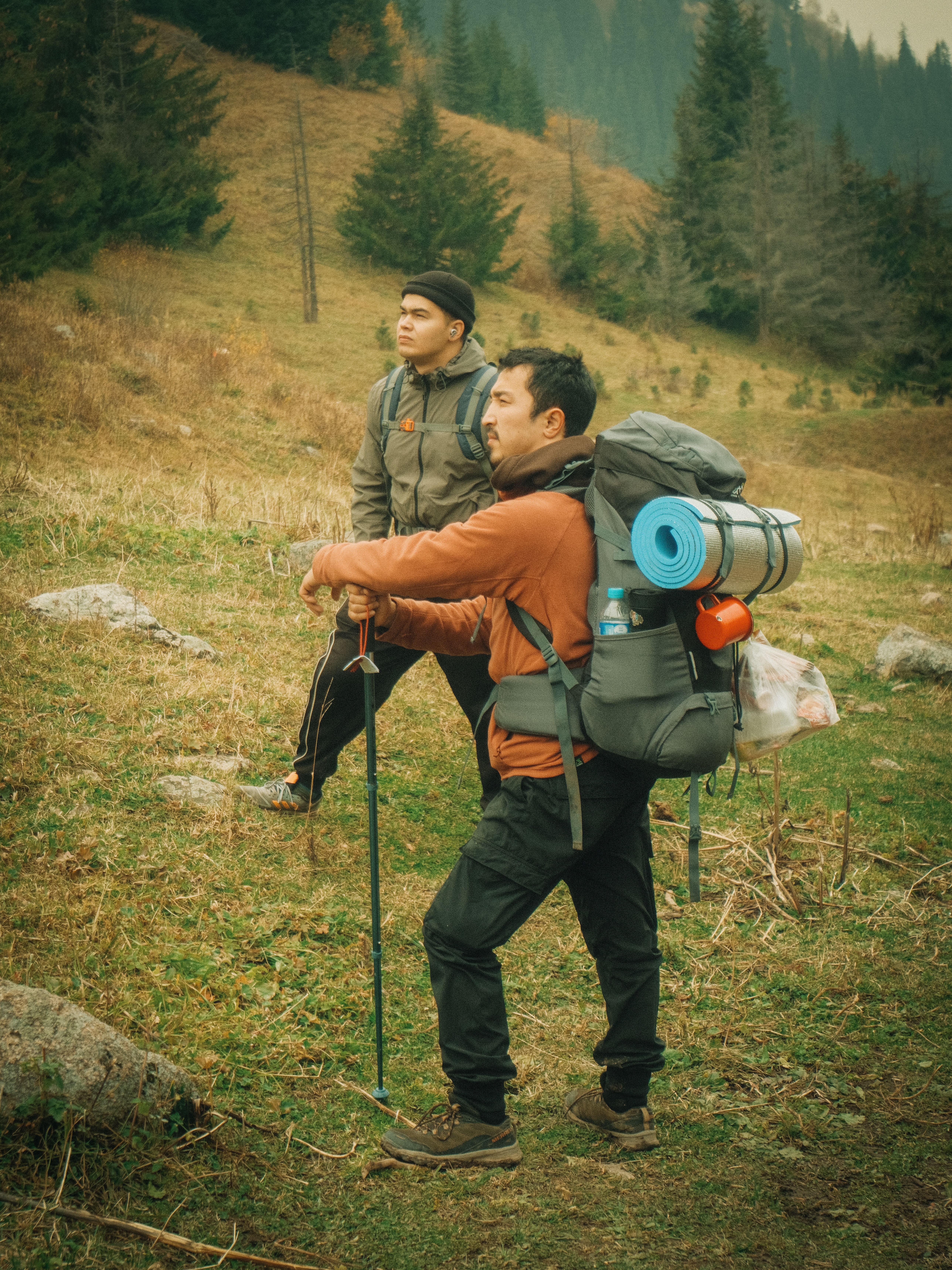 Two people walking uphill on a grassy trail with loaded backpacks and trekking poles