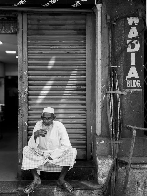Free Elderly man sitting outside a shop in an urban setting, black and white photo. Stock Photo