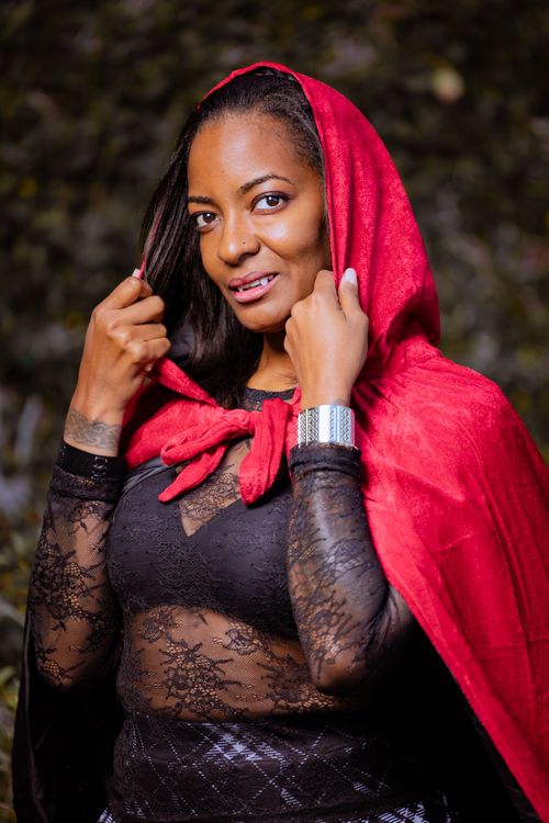 Free Stylish woman wearing a red hooded cape poses confidently in a natural forest setting. Stock Photo