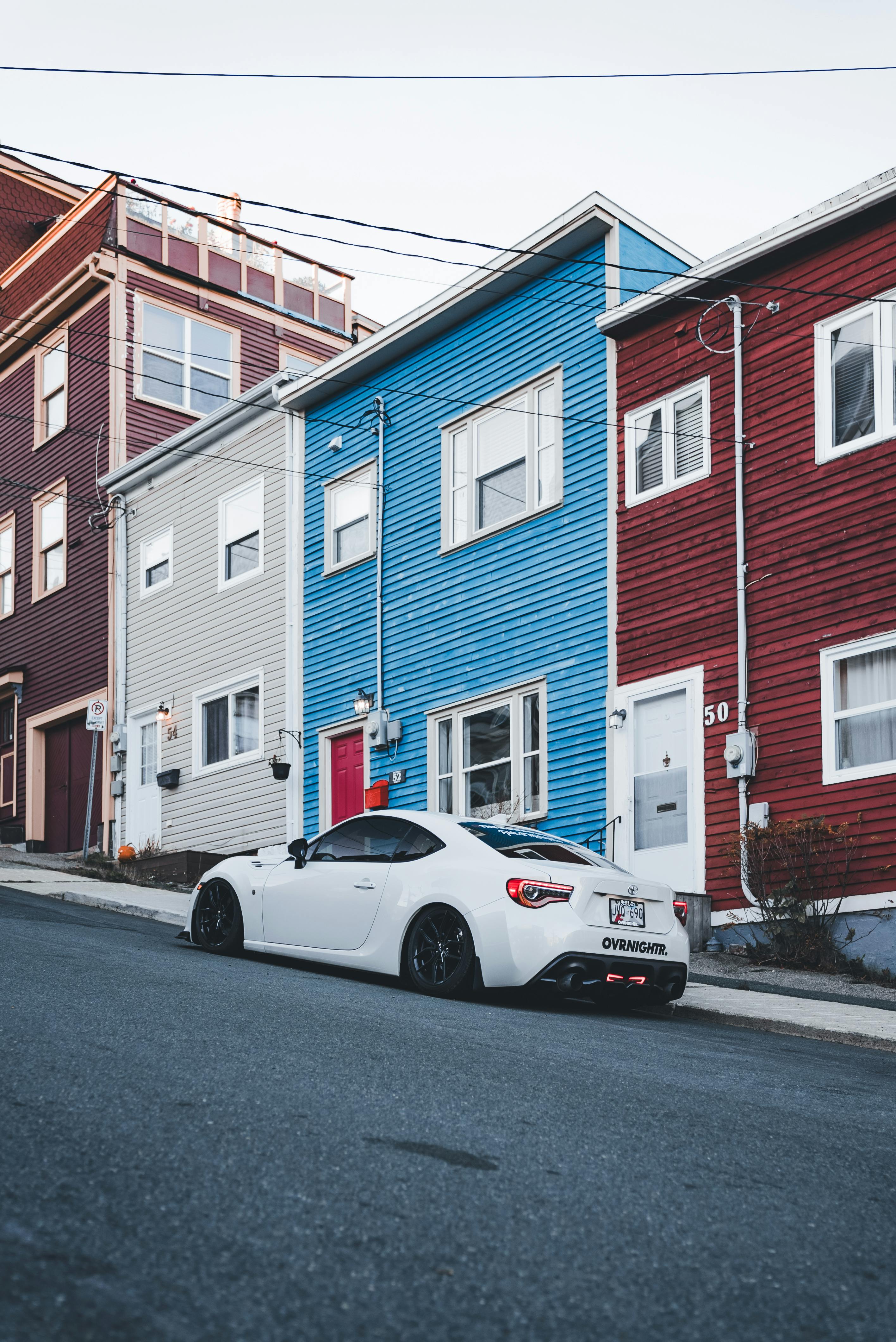 White sports car parked on a sloped city street with colorful wooden houses.