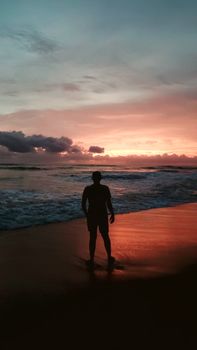 A silhouette of a person standing on a beach as the sun sets, creating a dramatic and serene scene.