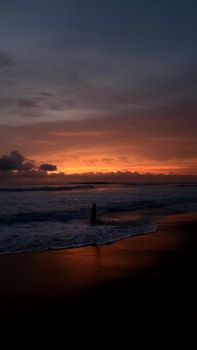 A silhouette stands by the ocean, framed by a vibrant sunset sky.