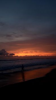 A lone silhouette walking along a beach with a vibrant sunset in the background.