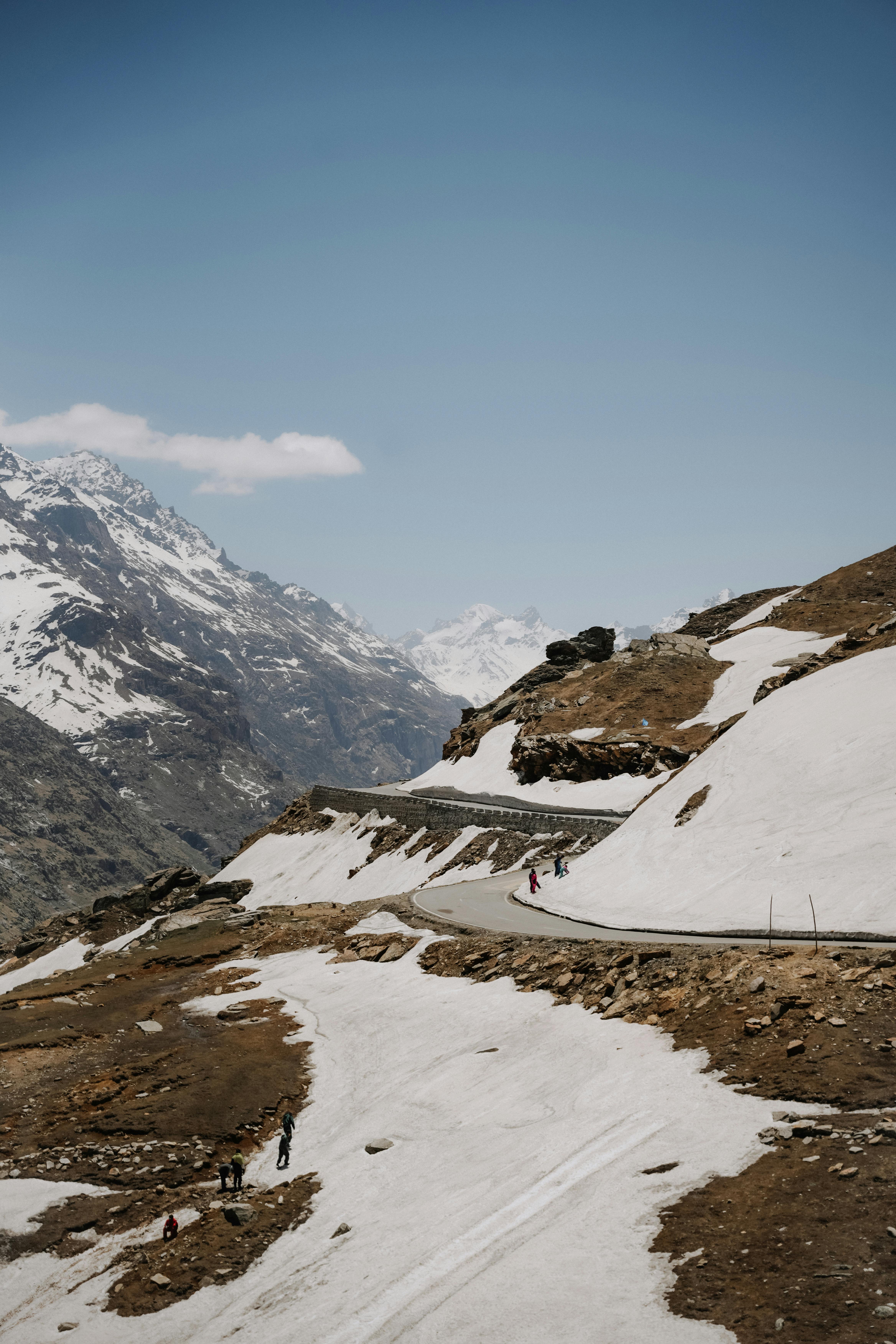 Stunning mountain landscape with winding road and snow-covered peaks under clear blue sky.