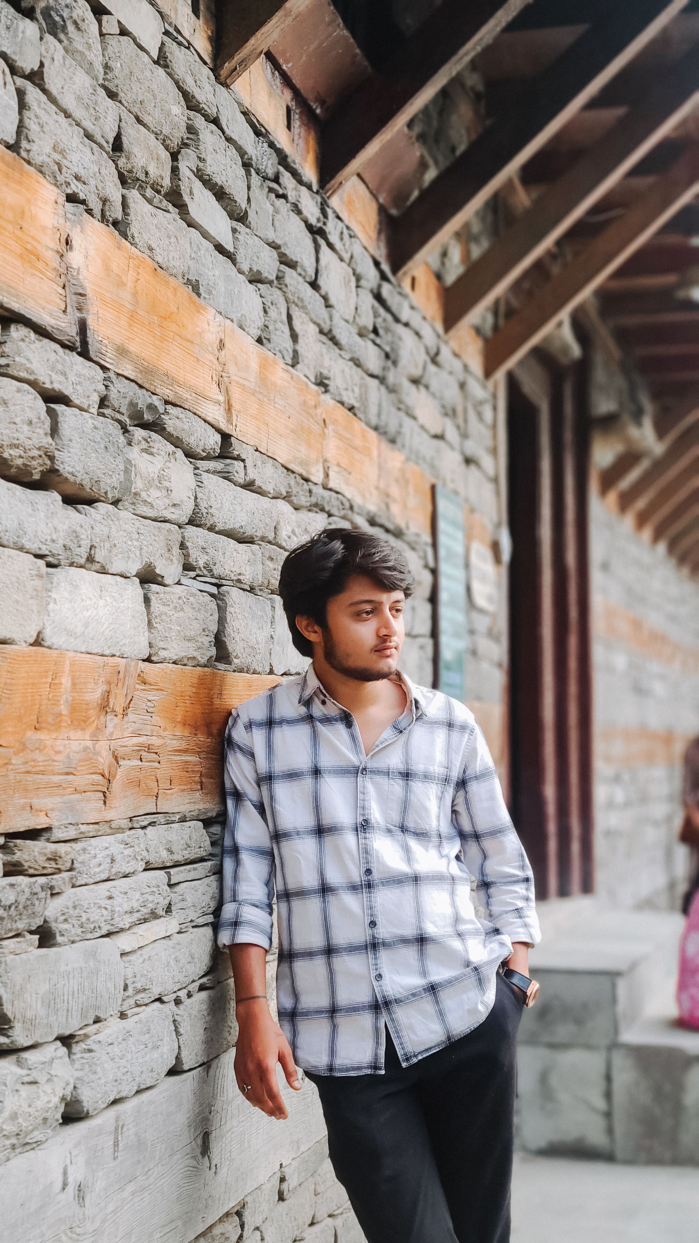 Young man in casual attire leaning against a rustic stone wall, embodying relaxed style and mood.