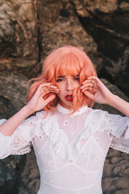 Portrait of a stylish woman with pink hair posing outdoors in a fashionable white dress.