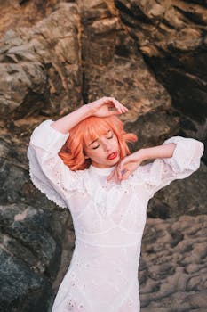 一位粉发美女身着白色连衣裙，在岩石背景前摆出姿势