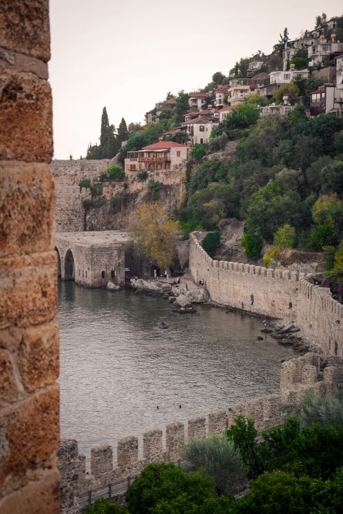 Free Scenic view of a historic fortress wall by the waterfront, surrounded by lush greenery and ancient architecture. Stock Photo