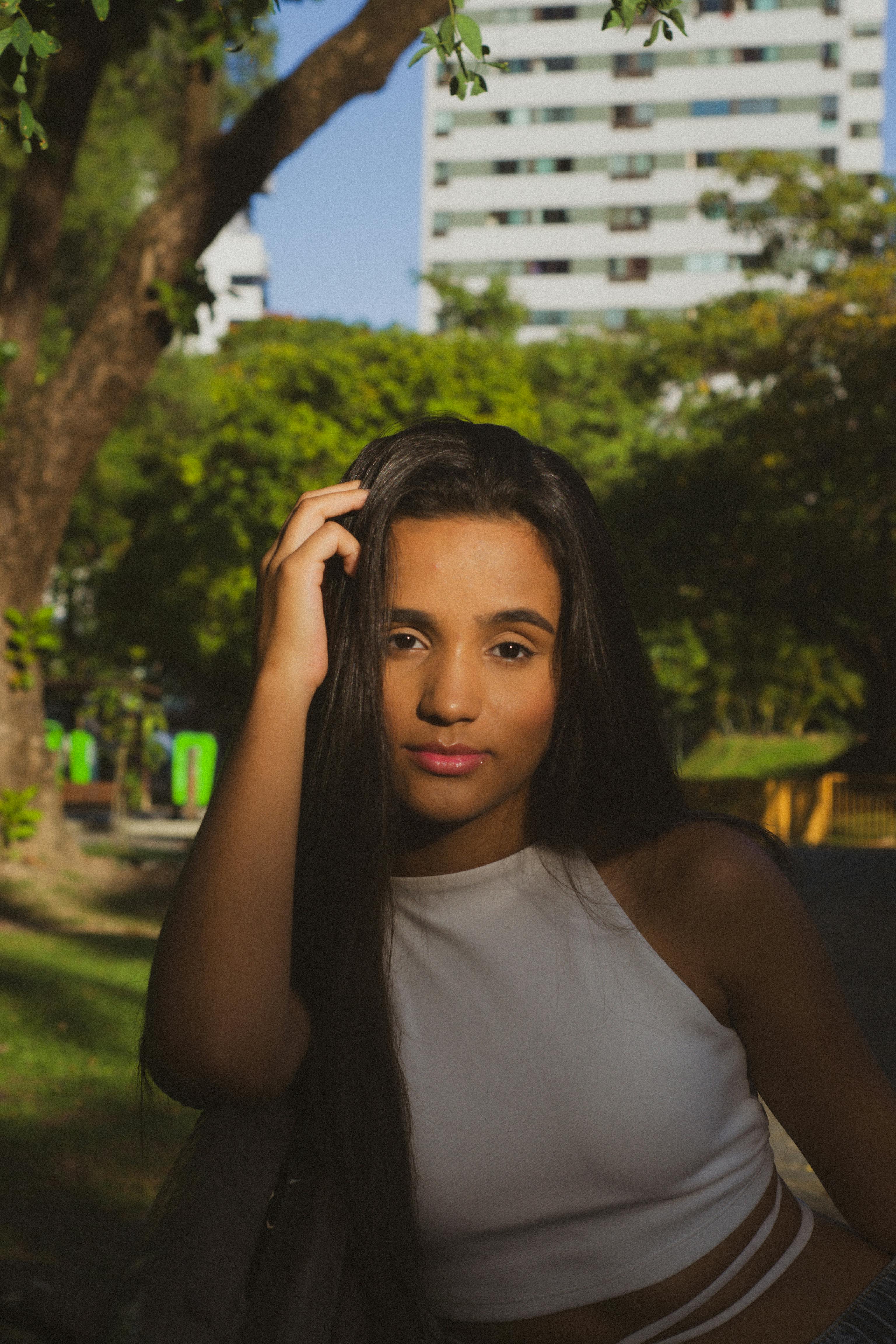 Portrait of a woman in a white top, posing outdoors with a sunny backdrop.