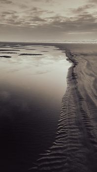 A serene black and white seascape featuring sculpted sand and calm waters at dusk.