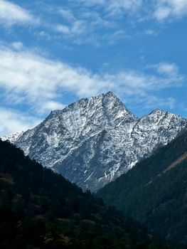 A breathtaking view of a snow-covered mountain peak surrounded by lush forests and a vivid blue sky.
