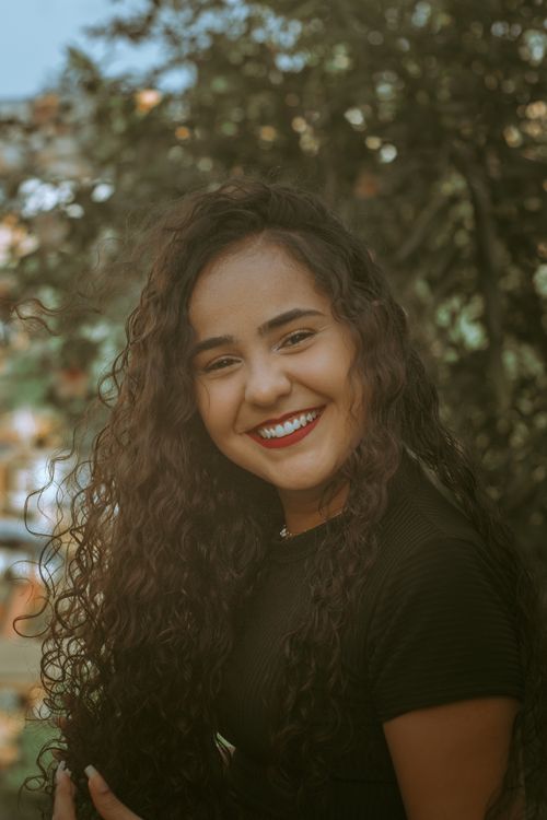 Free Portrait of a young woman smiling with confidence outdoors. Natural light and curly hair. Stock Photo