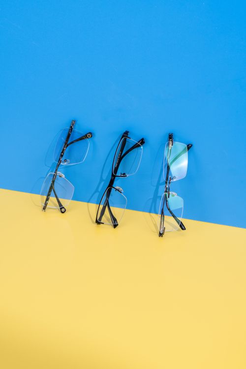 Free Three pairs of eyeglasses on a bold blue and yellow backdrop showcasing colorful lens reflection and modern design. Stock Photo
