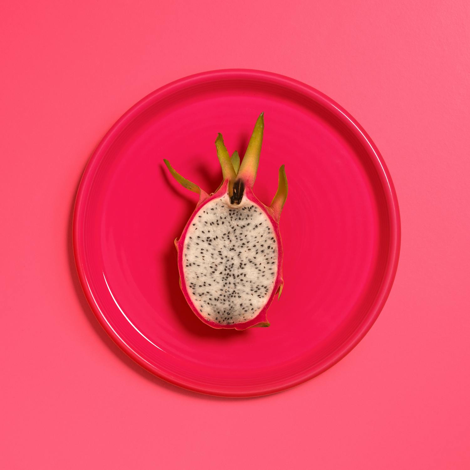 dragon fruit cut in half on bright pink plate w/ pink backdrop