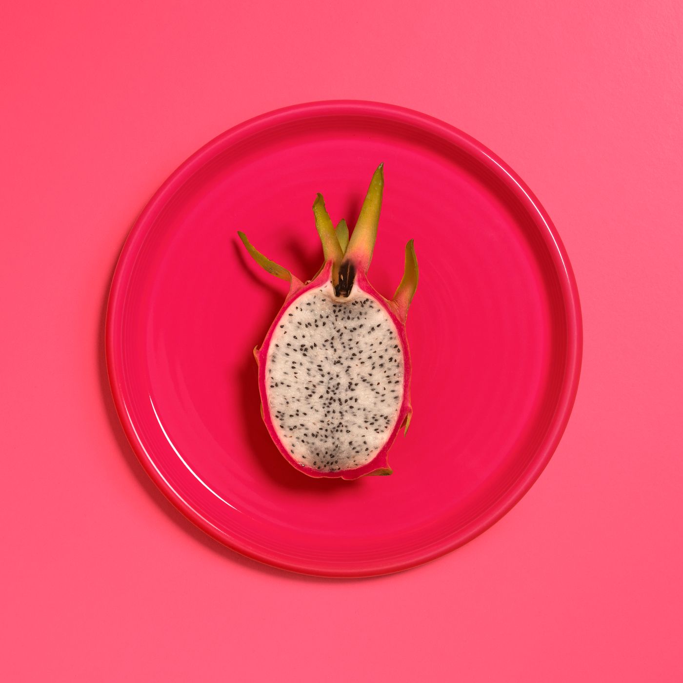 Sliced dragonfruit halves on a pink plate showing bright magenta flesh and black seeds