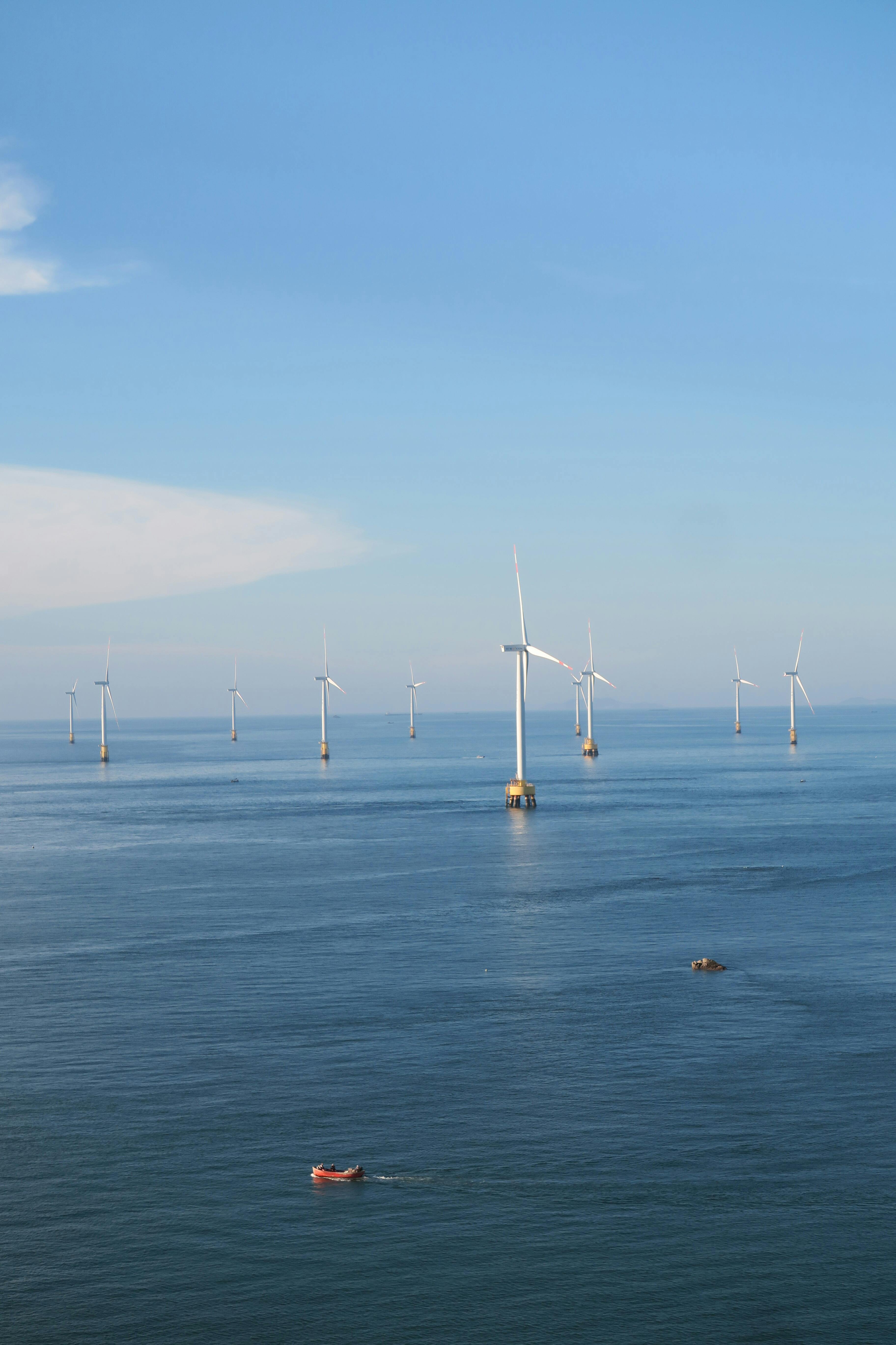 An expansive offshore wind farm with several wind turbines on a calm sea under a clear blue sky.