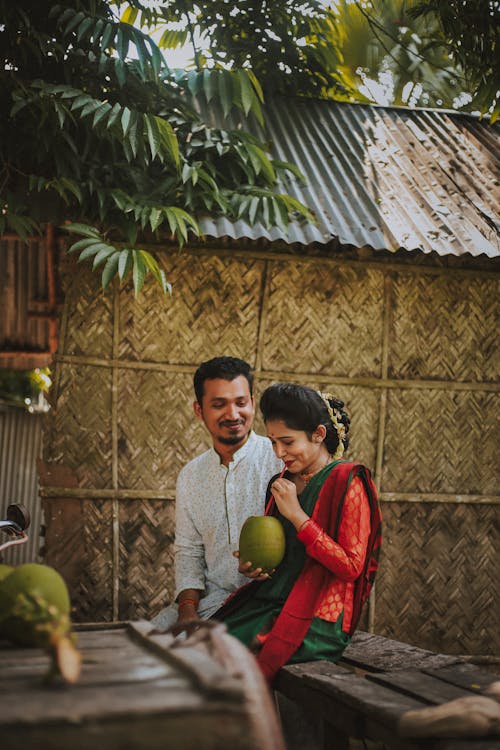 Man Seated Beside Woman Drinking from Coconut