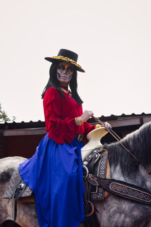 Free Woman in Day of the Dead attire with face paint riding a horse outdoors. Stock Photo