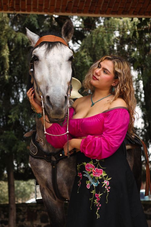 Free A woman in a vibrant dress poses elegantly with a horse against a natural backdrop. Stock Photo