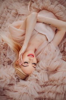 Blonde woman in a soft, ruffled dress lying gracefully with a joyful expression.