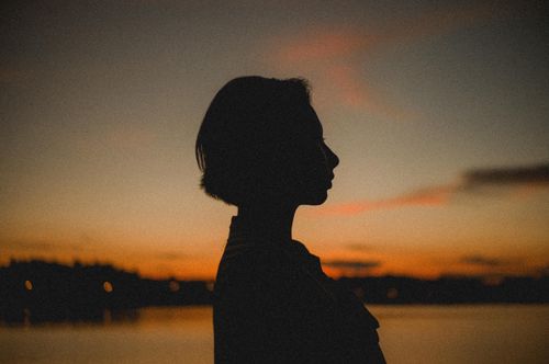 Free Artistic silhouette of a woman at sunset by a serene lake, showcasing calm and tranquility. Stock Photo