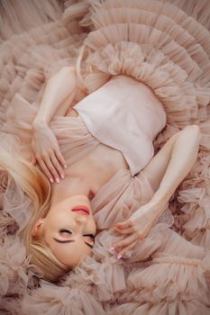 Woman in an elegant pink dress lying down surrounded by soft ruffles.