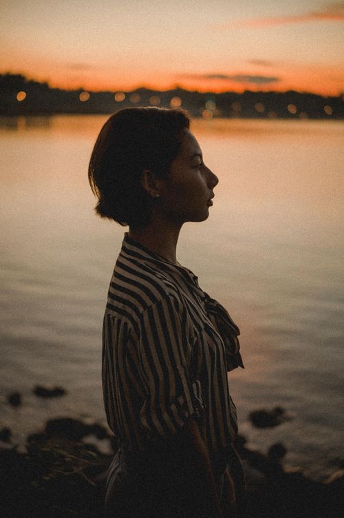 Free Captivating silhouette of a woman at a lakeside during sunset, featuring warm hues and serene vibes. Stock Photo