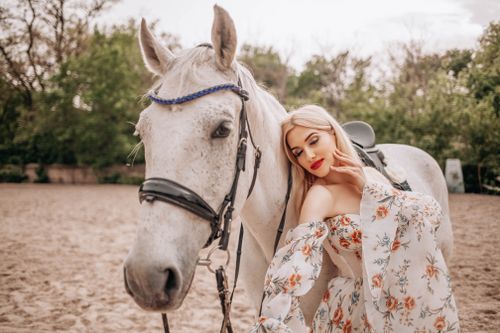 Free Charming scene featuring a woman in floral dress bonding with a white horse outdoors. Stock Photo