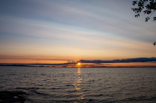 Serene lake sunset view with colorful sky and calm water reflecting sunlight.