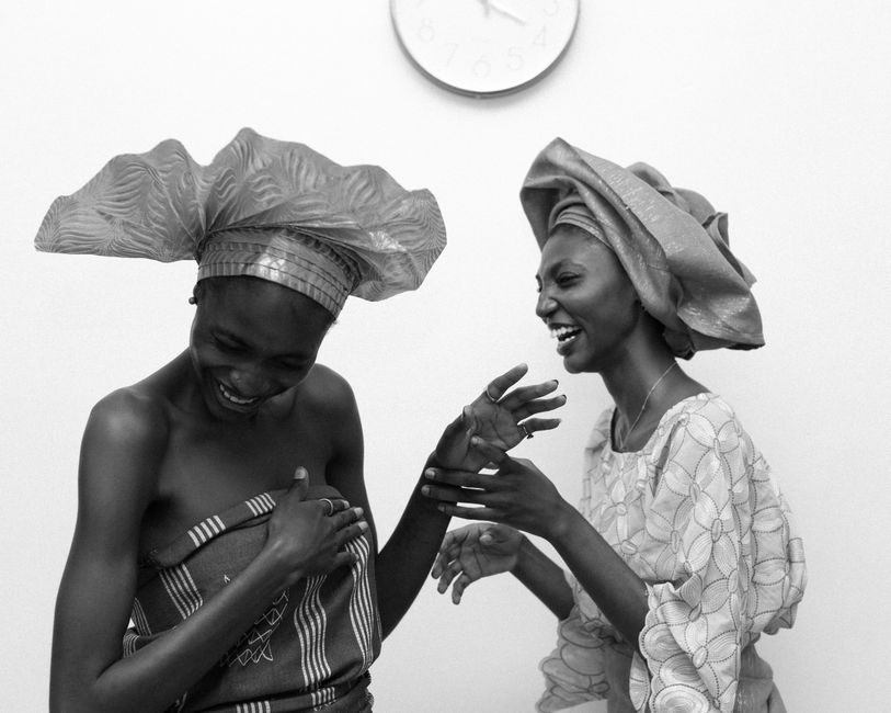 Two African women in traditional attire laughing together indoors. Captivating joy.