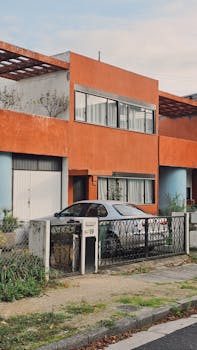 Modern house with orange facade and vintage car parked outside, showcasing urban architecture.