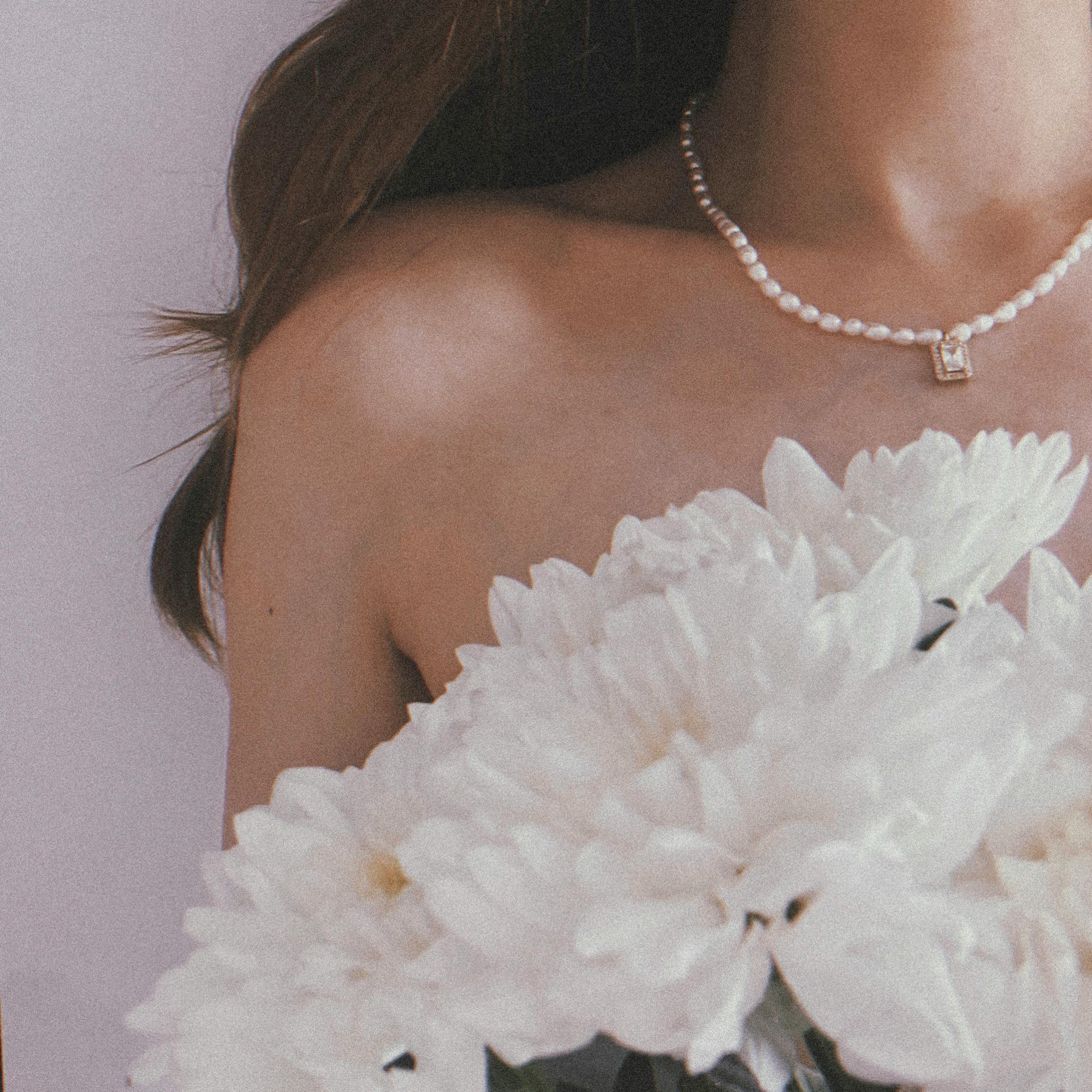 A woman in a pearl necklace holding white flowers, symbolizing elegance and purity.
