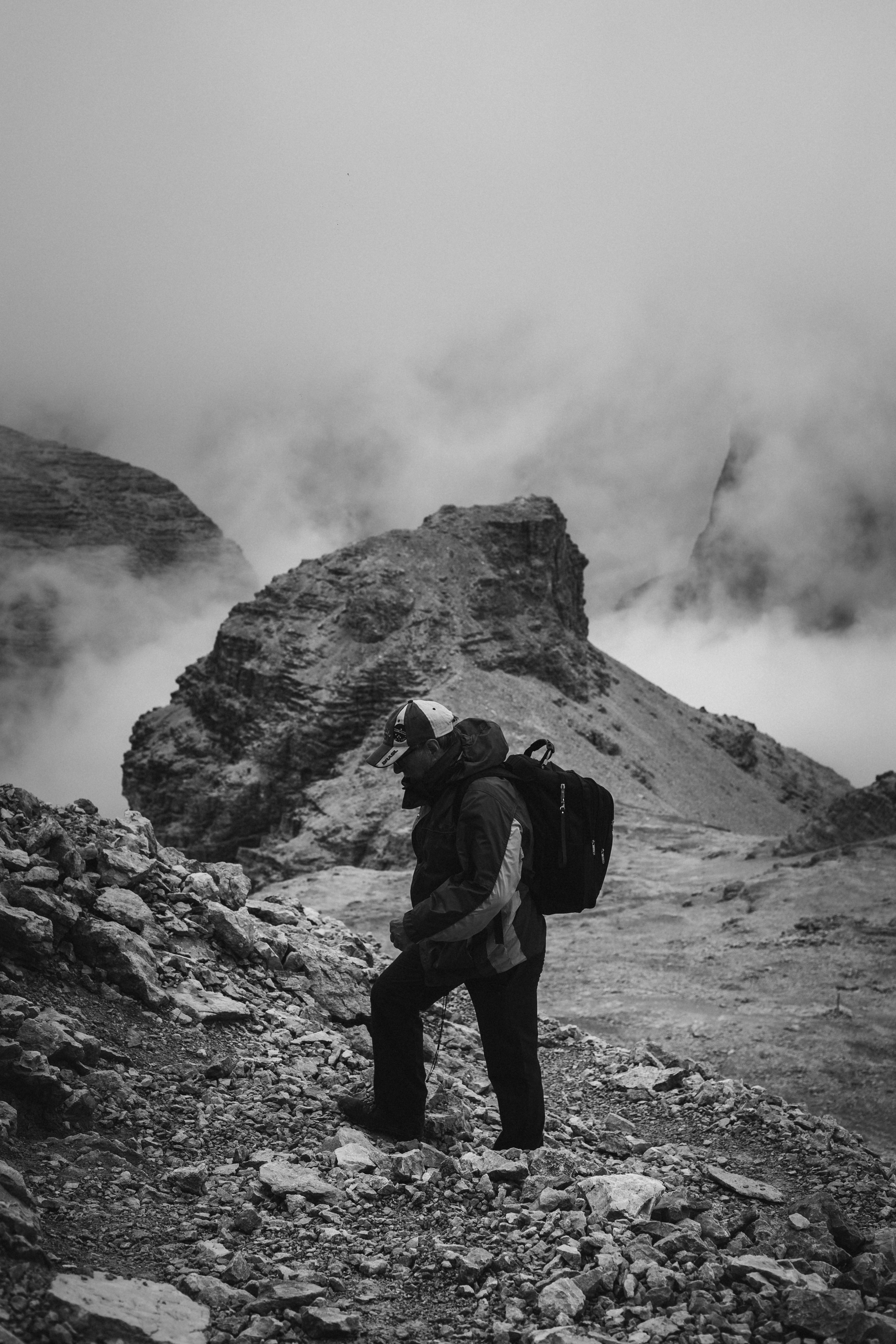 A lone hiker stands among rocky terrain and foggy mountains in Trentino-Alto Adige, Italy.