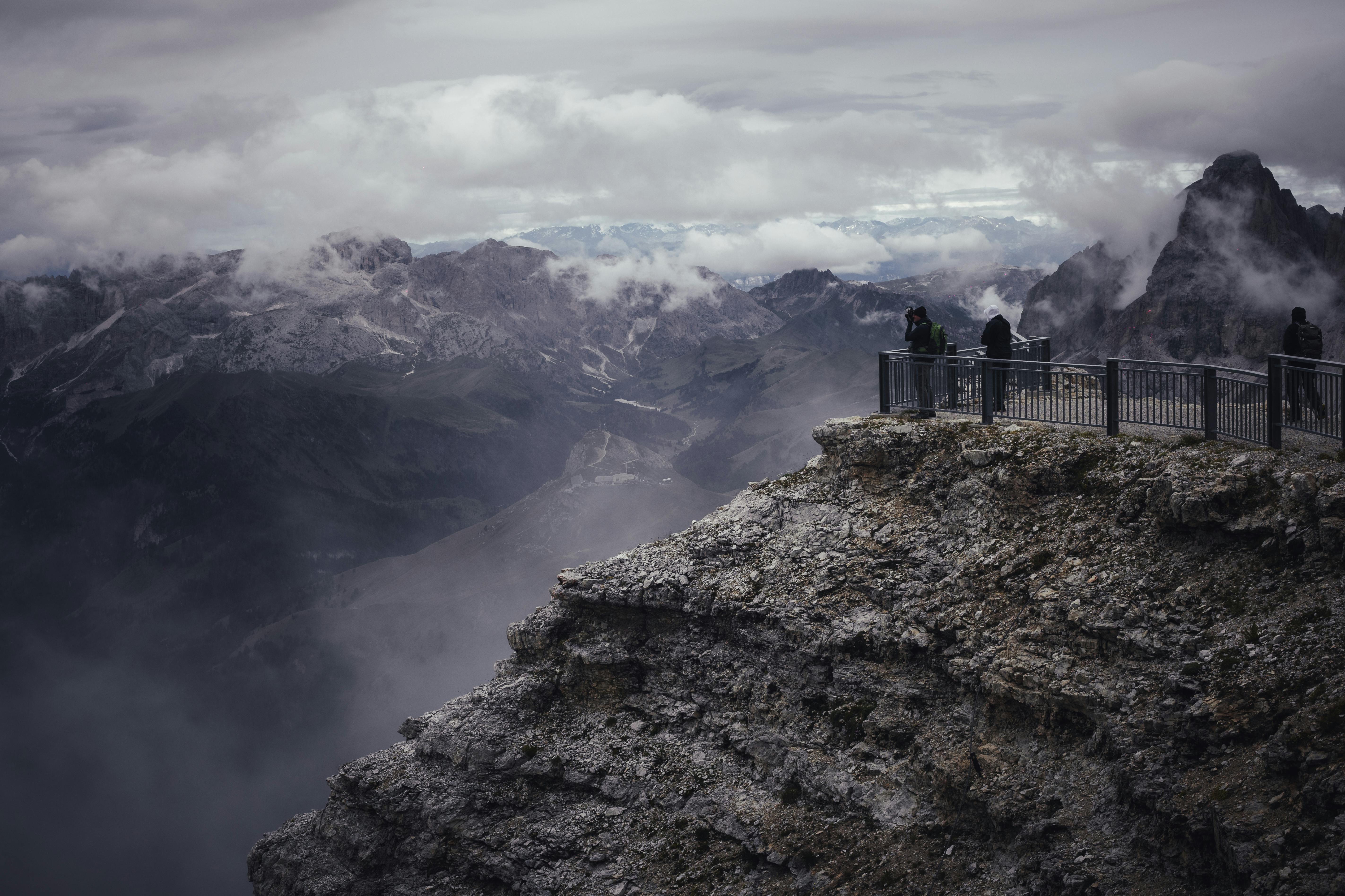 Tourists enjoying a dramatic mountain view from a high rocky cliff under cloudy skies.