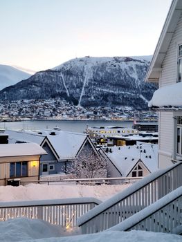 A serene winter landscape of Tromsø with snow-covered houses and fjord view.